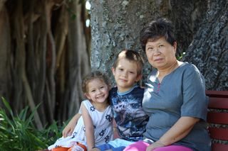  A grandmother seated on the ground next to a tree with her two young grandchildren seated next to her