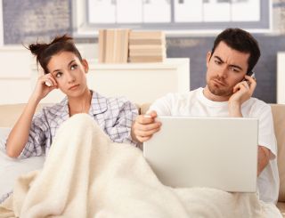 Man uses technology in bed while wife is bored