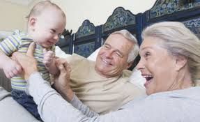 An older white couple playing with a little white baby on a bed