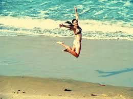 A woman in a bikini jumping on a beach