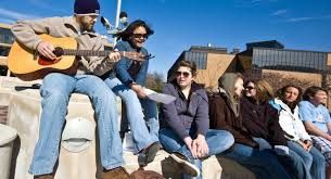 A group of college students sitting outside playing a guitar.