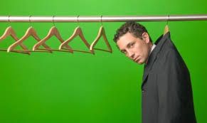  A white man wearing a suit hung from a hanger in a closet, green background