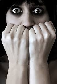Woman with dark hair and black smudges around eyes, fearfully covering her mouth