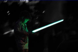 Small boy bathed in green light from toy lightsaber