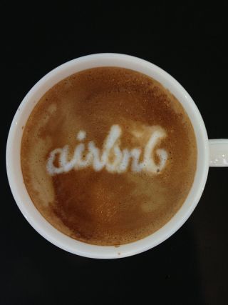 Old Airbnb logo written in white creamer in a cup of coffee.