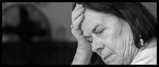 Black and white portrait of mature woman with head bowed in pain.