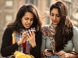 Two female friends standing side by side, using their cell phones