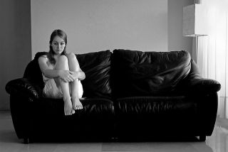 Sad woman sitting on when end of a couch with her knees folded up to her chest